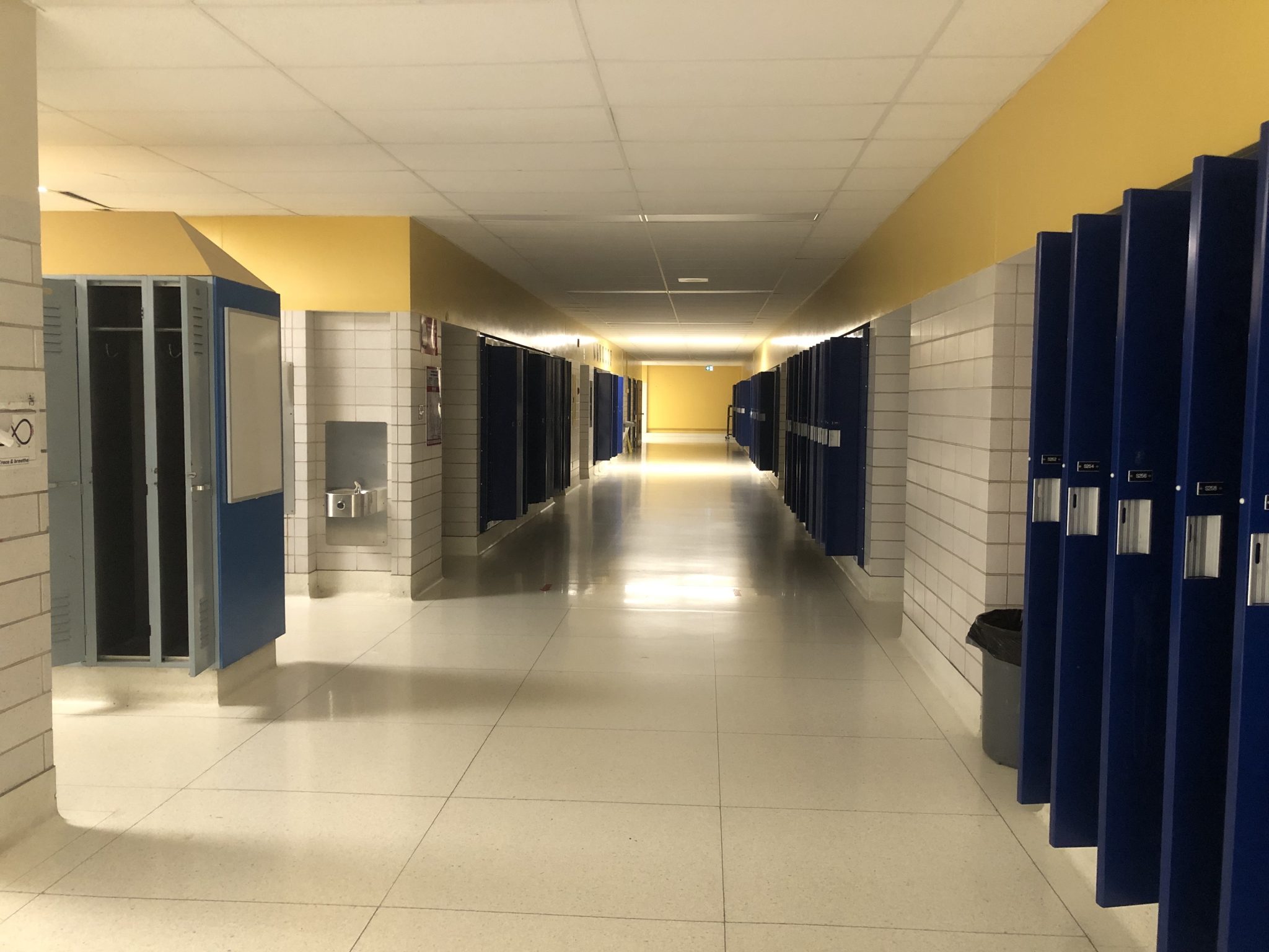 An empty high school hallway, partially darkened, with all the locker doors open.