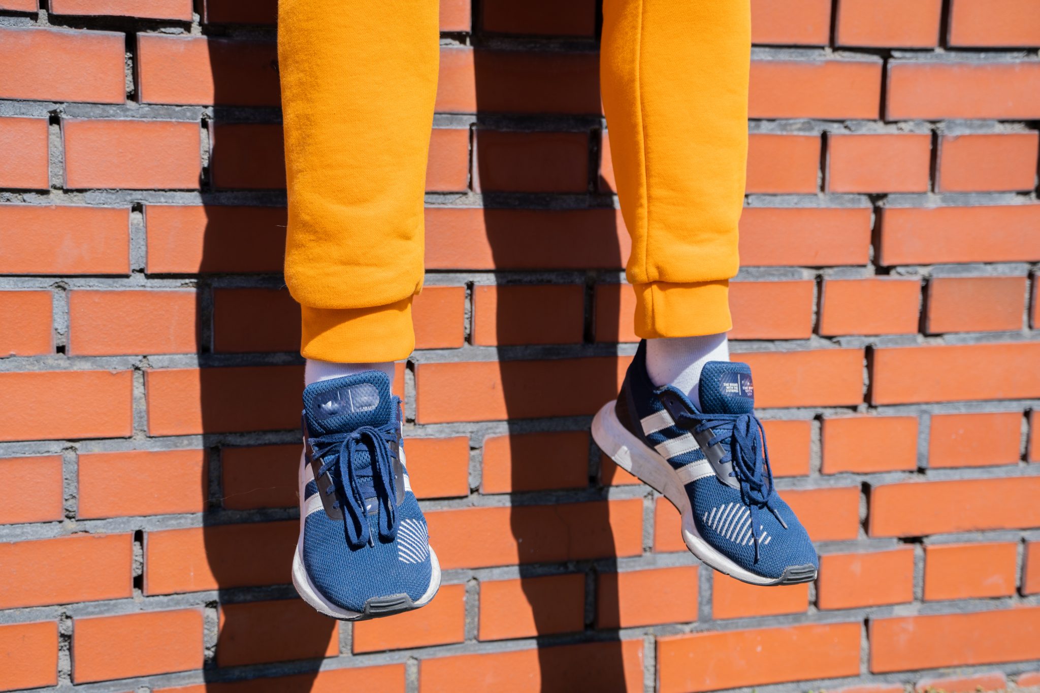 Casually dressed man sitting on a brick wall. He's wearing trendy sweatpants and stylish sneakers. This photo encapsulates urban lifestyle, street fashion, and modern leisure. Ideal for themes around city life and men's fashion.